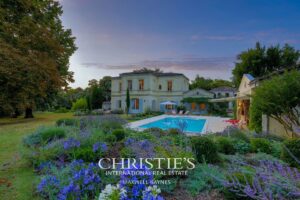 Grande maison élégante avec une piscine et un jardin fleuri au crépuscule.
