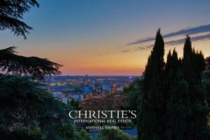 Vue panoramique d'une ville au crépuscule, entourée de cyprès sombres et d'arbres, sous un ciel aux couleurs dégradées.