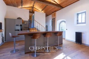Cuisine moderne avec un îlot central en bois, chaises hautes, et plafond en bois apparents.