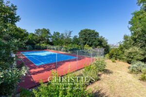 Un court de tennis extérieur entouré de végétation, sous un ciel bleu clair.