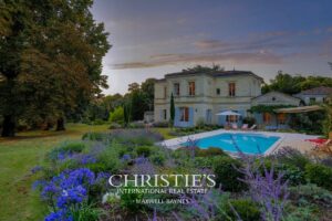 Une élégante maison avec piscine, entourée d'un jardin fleuri et de grands arbres, baignée par la lumière du crépuscule.