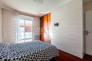Une chambre lumineuse avec un lit à motifs noirs et blancs, de grandes fenêtres et des murs clairs.
