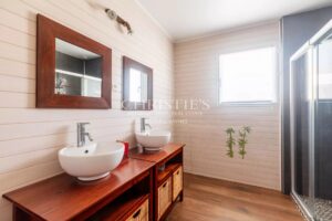 Salle de bains moderne avec deux lavabos, miroirs en bois et douche, éclairée par une fenêtre.