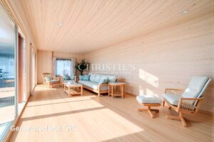 Un salon spacieux en bois clair avec de grandes fenêtres, des meubles en bois et un canapé confortable.