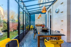 Une véranda moderne avec une grande table noire, des chaises jaunes et un plafond en verre, offrant une vue sur le jardin extérieur.