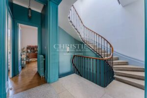 Un escalier élégant avec une rampe en bois et des murs bleus, à côté d'une pièce avec un parquet en bois.