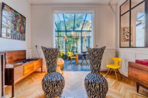 Un intérieur moderne et coloré avec des chaises à motif zébré, une grande fenêtre offrant une vue sur la végétation, et des touches de jaune vif dans les meubles.