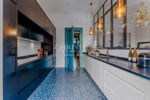 Cuisine moderne avec des armoires noires et blanches, un sol carrelé bleu, et des suspensions lumineuses.