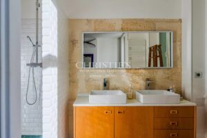 Salle de bain moderne avec double vasque, miroir rectangulaire et douche carrelée blanche.