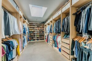 A spacious, well-organized walk-in closet with neatly arranged clothes and shoes on open shelving, illuminated by a skylight.