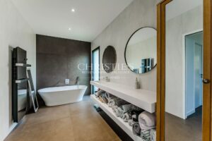 Modern bathroom with a freestanding bathtub, round mirrors, and open shelves holding towels.