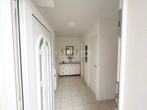 Un couloir blanc avec un carrelage clair, décoré d'une commode et d'un miroir au fond.