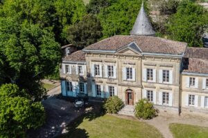 A historic chateau with a conical tower, surrounded by lush greenery, featuring a symmetrical facade and large windows.